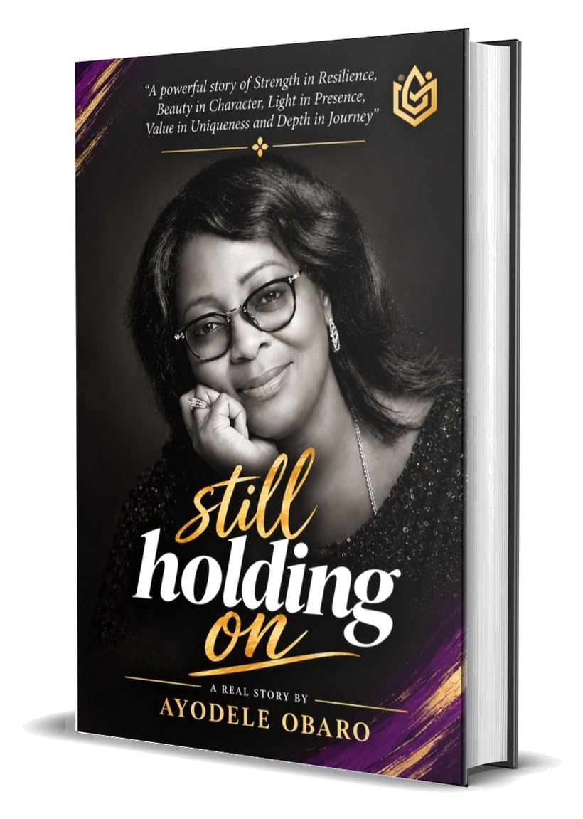 Hardcover copy of Still Holding On by Ayodele Obaro, with a black and purple cover and gold lettering