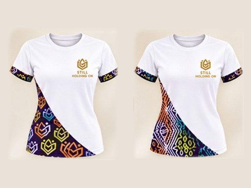 Women's white T-shirts with the Still Holding On emblem and Ankara-inspired fabric panels